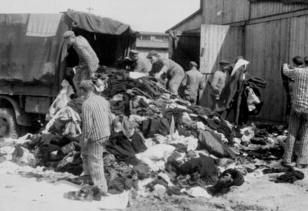 Więźniowie Auschwitz-Birkenau pracujący przy sortowaniu ubrań (domena publiczna).