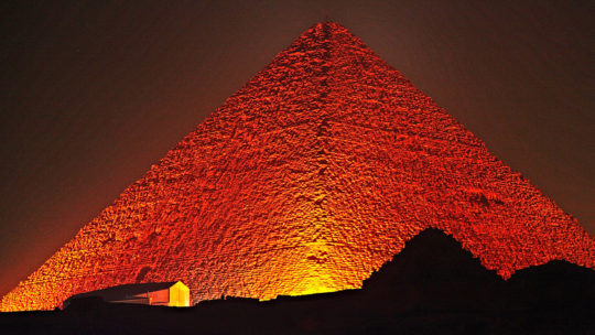 Nocne oświetlenie wielkiej piramidy w Gizie. Na szczycie widoczny zarys drewnianego masztu