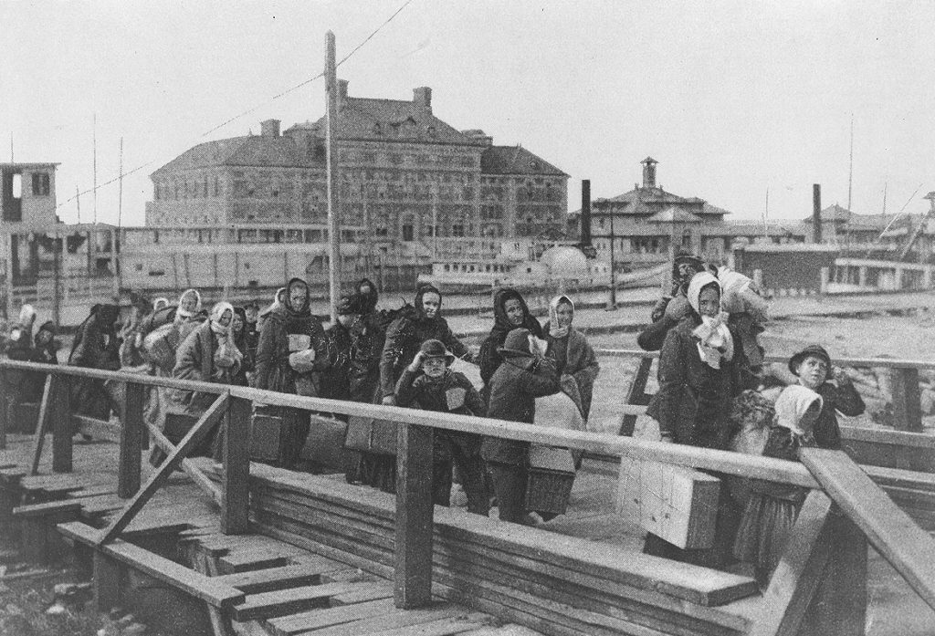 Imigranci na Ellise Island. Zdjęcie z 1902 roku (domena publiczna).