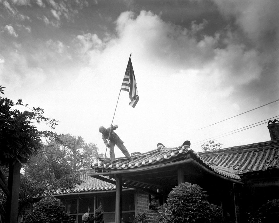 Żołnierz piechoty morskiej wznosi amerykańską flagę nad konsulatem USA w Seulu. 27 września 1950 roku (domena publiczna).