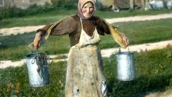 Wiejska kobieta niosąca wodę z użyciem koromysła.